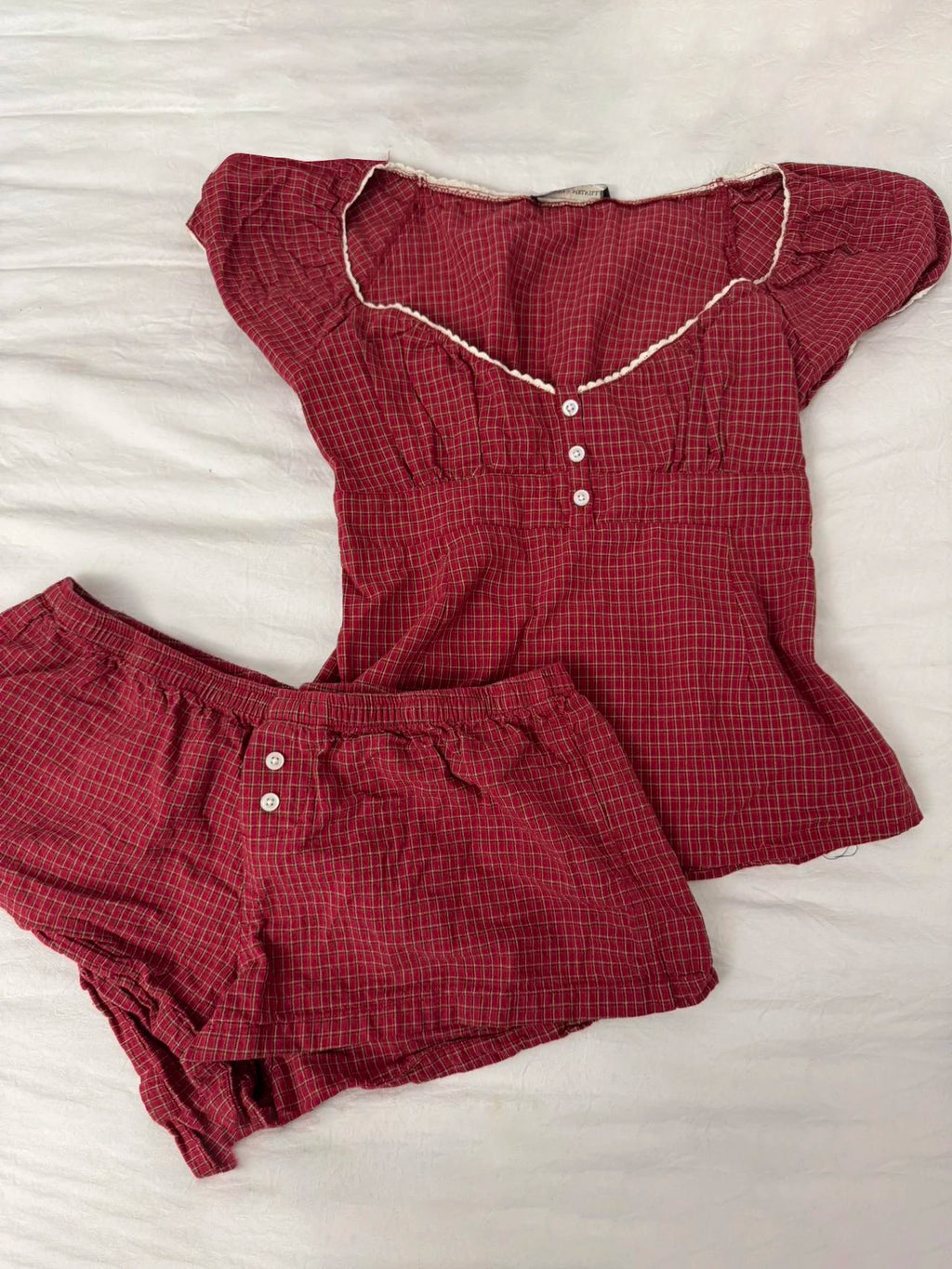 Conjunto de verano para mujer de 2 piezas, compuesto por una blusa de cuadros rojos con mangas abullonadas y detalle de amarre, acompañada de shorts de algodón con botones y cintura elástica. Fresco, cómodo y perfecto para un look femenino y moderno.
