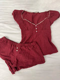 Conjunto de verano para mujer de 2 piezas, compuesto por una blusa de cuadros rojos con mangas abullonadas y detalle de amarre, acompañada de shorts de algodón con botones y cintura elástica. Fresco, cómodo y perfecto para un look femenino y moderno.