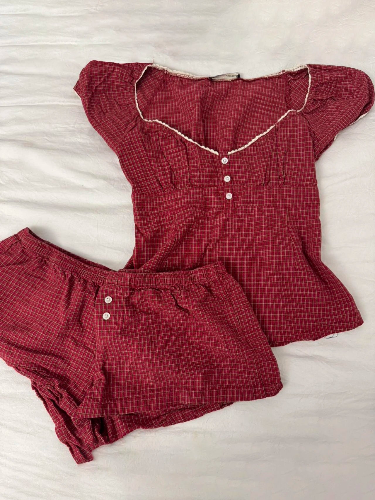 Conjunto de verano para mujer de 2 piezas, compuesto por una blusa de cuadros rojos con mangas abullonadas y detalle de amarre, acompañada de shorts de algodón con botones y cintura elástica. Fresco, cómodo y perfecto para un look femenino y moderno.